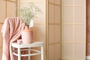 Odadaki perdenin yanında mum ve vazolu sandalye.