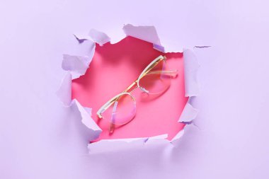 Renkli arka planda yırtık kağıt yoluyla görünen gözlük
