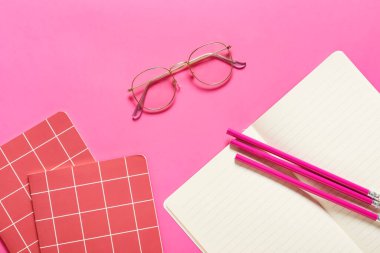 Renkli arka planda not defterleri ve kalemleri olan şık gözlükler