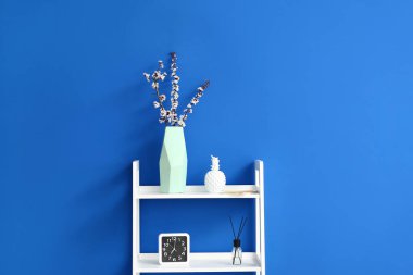 Renk duvarının yanındaki rafta çiçek açan bahar dalları olan vazo.