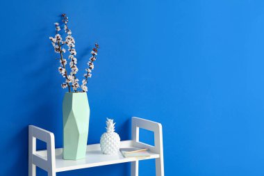 Renk duvarının yanındaki rafta çiçek açan bahar dalları olan vazo.