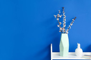 Renk duvarının yanındaki masada çiçek açan bir vazo.