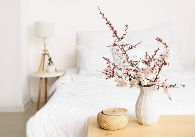 Yatağın başucundaki bankta çiçek açan güzel dalları olan vazo.