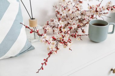Çiçek açan güzel dallar, bir fincan çay, oda spreyi ve çekmecelerin üstündeki yastık.
