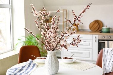 Mutfaktaki yemek masasında çiçek açan güzel dalları olan vazo.