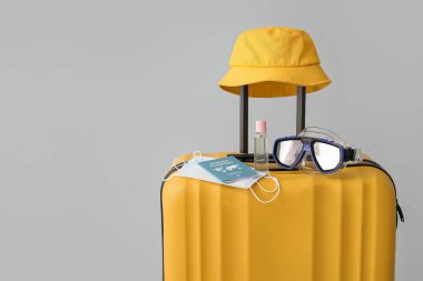 Bağışıklık sistemi pasaportu, tıbbi maskeler, dezenfektan ve gri arka planda plaj aksesuarları olan bavullar.