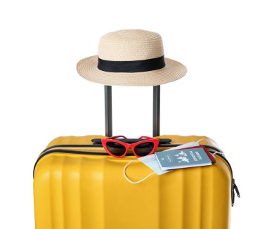 Beyaz arka planda bağışıklık pasaportu, sağlık maskesi, şapka ve güneş gözlüğü olan bavul.