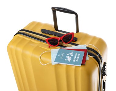 Beyaz arka planda bağışıklık pasaportu, sağlık maskesi ve güneş gözlüğü olan bavul.