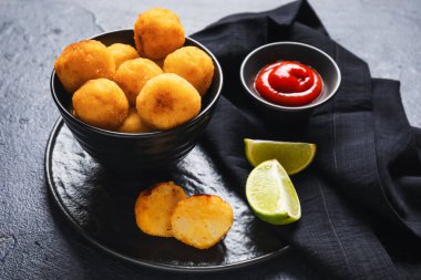 Kızarmış patates topları ve koyu arkaplanda domates sosu olan tepsi.