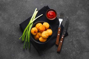 Koyu arkaplanda kızarmış patates topları ve domates sosu olan bir kase.