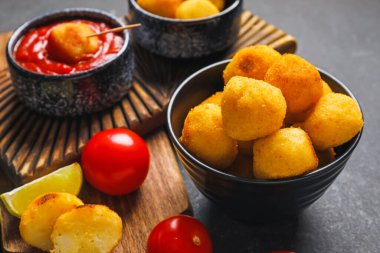 Koyu arkaplanda kızarmış patates topları olan bir kase.