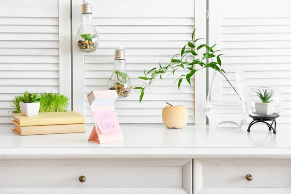 Tear-off calendar, books and houseplants on table in room