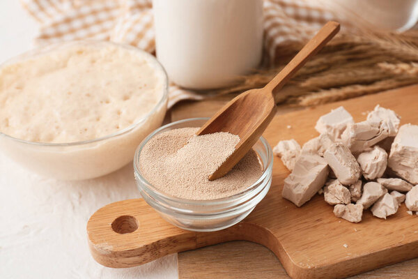 Деревянная доска со свежими и сухими дрожжами на светлом фоне