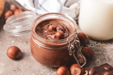 Lezzetli çikolata ezmeli kavanoz ve gri arka planda fındık.