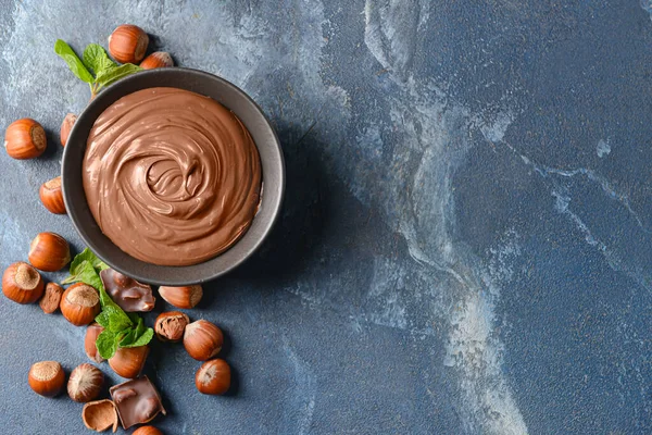 Bowl with tasty chocolate paste and hazelnuts on color background