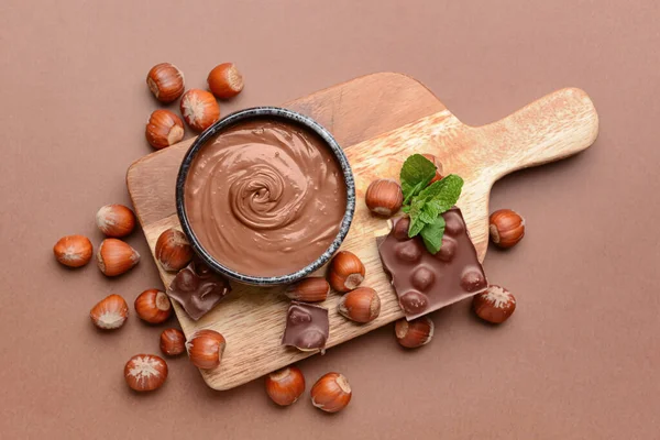 Bowl with tasty chocolate paste and hazelnuts on color background