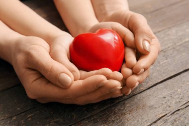 Ahşap arka planda kırmızı kalpli kadın ve çocuğun elleri, yakın plan.