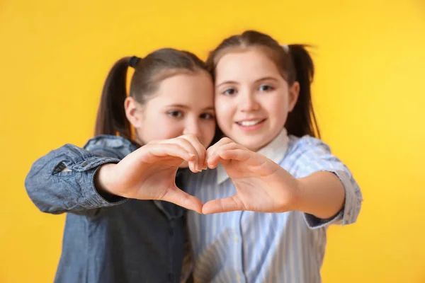 可愛いです双子の女の子作る心形とともに彼らの手上の色の背景 — ストック写真