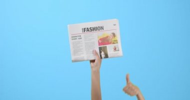 Renk arkaplanında başparmak gösteren gazeteli eller