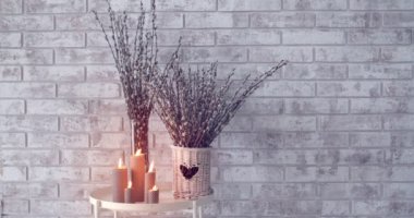 Pussy willow branches and burning candles on table near brick wall