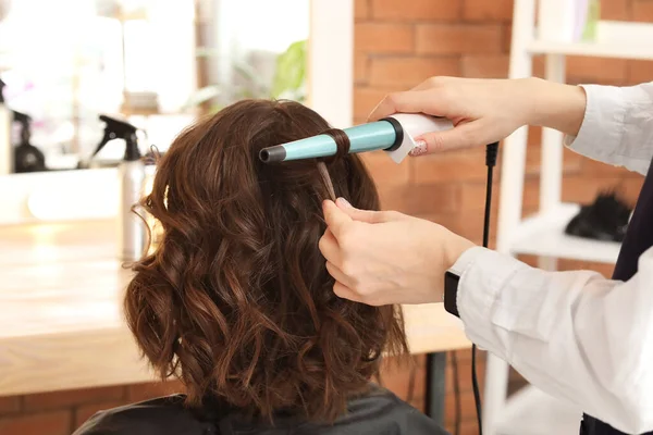 Female hairdresser curling hair of client in beauty salon