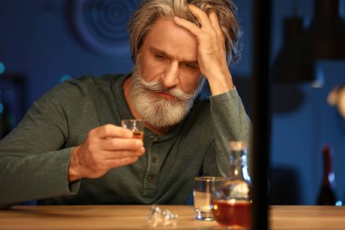 Drunk senior man with glass of whiskey late in evening at home