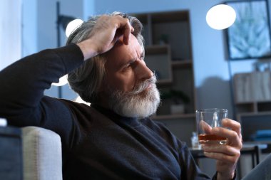 Senior man with glass of drink late in evening at home