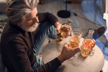 Drunk senior man with glass and bottle of drink late in evening at home