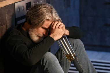 Drunk senior man with bottle of drink in kitchen at night