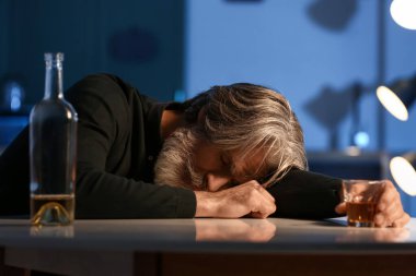 Unconscious drunk senior man with glass of drink in kitchen at night
