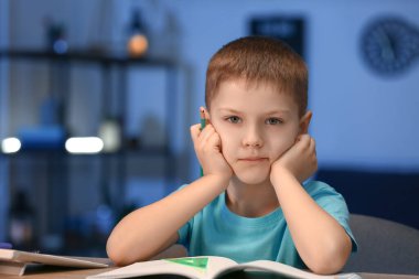 Küçük çocuk akşam geç saatte evde ödev yapıyor.
