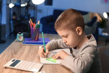 Küçük çocuk akşam geç saatte evde ödev yapıyor.