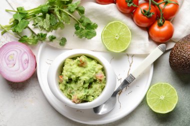 Hafif arka planda lezzetli guacamole, limon, domates ve soğanlı kase.