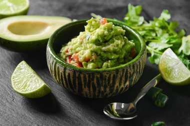 Lezzetli guacamole, avokado ve koyu arkaplanda limon, yakın plan.