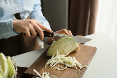 Woman cutting fresh cabbage on table in kitchen, closeup