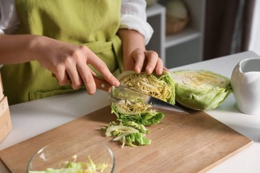 Woman cutting fresh cabbage on table in kitchen, closeup