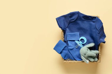 Basket with baby clothes, toy and pacifier on color background