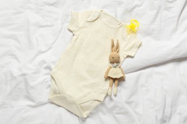Baby bodysuit, toy and pacifier on bed