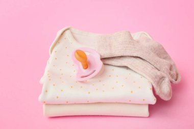 Renk arkaplanına bebek kıyafetleri ve emzik yığını