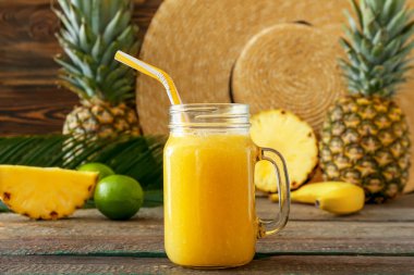 Mason jar of tasty pineapple smoothie and hat on wooden background
