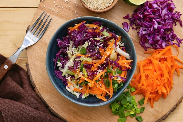 Bowl with tasty cabbage salad and ingredients on wooden table