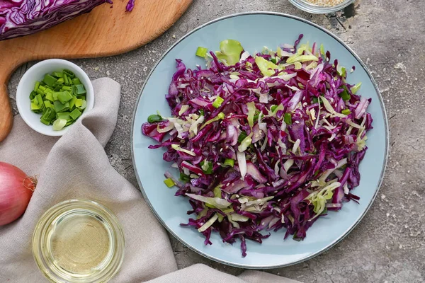 Plate with tasty cabbage salad and ingredients on grunge background