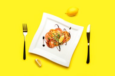 Plate with tasty tomato carpaccio, lemon and cutlery on color background