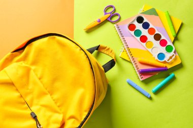 Renk arkaplanında kırtasiye malzemesi olan okul çantası