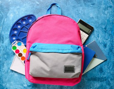 Renk arkaplanında kırtasiye malzemesi olan okul çantası