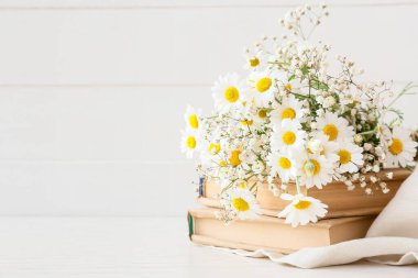 Bir buket güzel papatya çiçeği ve hafif ahşap zemin üzerine kitaplar, yakın plan.