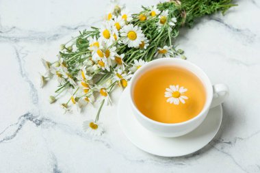 Bir fincan çay ve bir buket güzel papatya çiçeği açık arkaplanda.