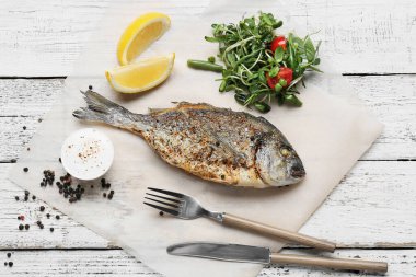 Kızarmış dorado ve beyaz ahşap arka planda salata.