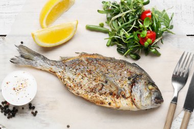 Kızarmış dorado ve beyaz ahşap arka planda salata.