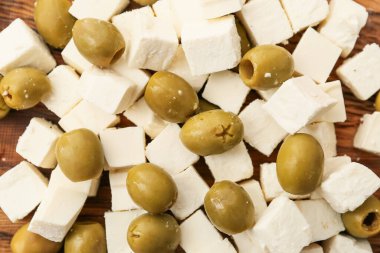 Lezzetli peynir parçaları ve ahşap zemin üzerinde yeşil zeytinler.